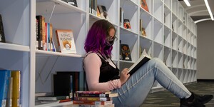 Young woman sitting on the floor among the book shelves with a stack of books next to them.