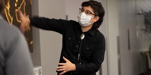 A librarian wearing a mask gestures at the screen on the wall.