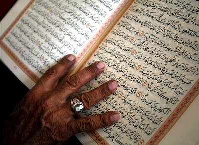 Elderly man touches pages of Quran as he reads it after noon prayers
