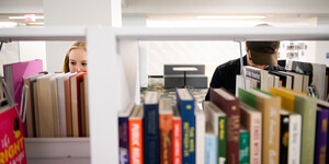 Two students looking through bookshelves at the library
