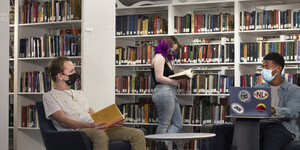Three students in the library talking and looking at books