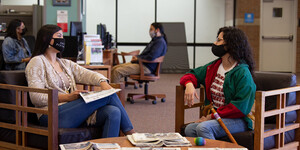 Two Native American women sit and speak together while wearing masks for safety in the Labriola center.