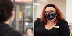 A person wearing a name tag smiles at a library patron while wearing a mask.