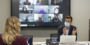 Two people talking with a Zoom meeting happening on a screen behind them