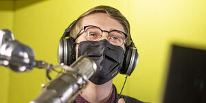 Male student in a podcasting room with a large microphone in the foreground.