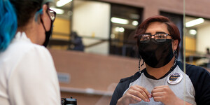 A student worker greets a library patron while wearing a mask.