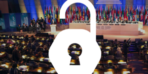 an open access padlock image is superimposed over a dark theater, with a panel of speakers on the stage in front of a UNESCO logo and international flags