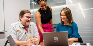 Three people talking and looking at a laptop