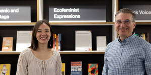 Two people smiling for the camera in front of a book shelf display