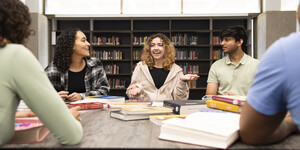 Group of students talking at a table with bookshelves in the background