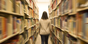 Person walking through book stacks with shelves slightly blurred