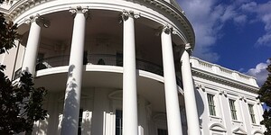 a view of the outside columns of the central portico of the White House in Washington, D.C, with a deep blue sky behind.