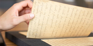 A hand holds a written manuscript page as it is being turned over.