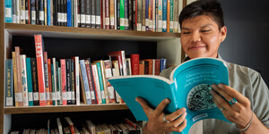 Student holding a book in from of open stacks