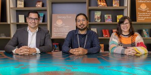 Three people sitting at a table smiling for the camera with a bookshelf in the background