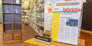 Tabletop display of newsletters with open stacks shelving in the background