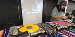 A local Indigenous DJ spins records with a movie streaming in the background.