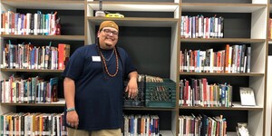 Student standing in front of bookshelves and a case of vinyl records smiling for the camera