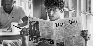 A student is seated at a table reading Thunderbird’s student newspaper, called Das Tor.