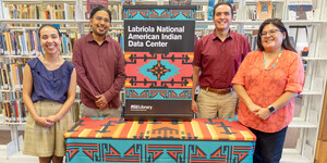 Employees stand behind a welcome table draped with Labriola National American Indian Data Center banners.