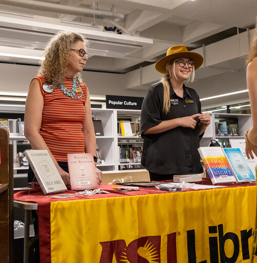 Two library employees speaking with student at a welcome event.