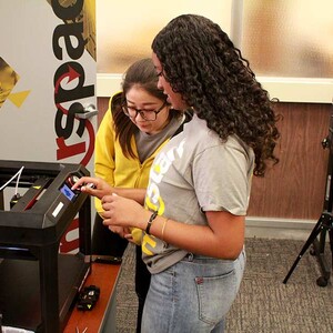 Two students check the settings on a 3D printer.