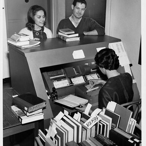 A library worker checks books out for students using a computer punch card system.