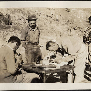 Buzz Holmstrom watches some mapwork at foot of Travertine Rapids, Ian Campbell and Johnny Maxon at the table [Nov. 1937]
