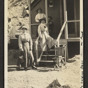 Black and white print of three women, one man and one child at a Hermit Creek Camp cabin. Handwritten annotation, "Annie Goodenough took the picture. Will Shope holding babe Mary on porch".