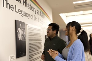 Two people viewing an exhibit display featuring Dr. Eugene Grigsby.