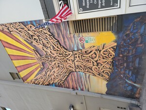 Photo of fist mural Breeze showed the Labriola Center. The Phoenix is made up of golden/copper spirals and rises from the city, which is covered in a blue hue from the rising and setting sun. "South Mountain" is to the left with the electrical towers standing erect, with their lights atop, barely brushing the sky..