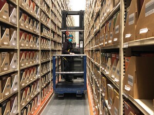 A person driving a forklift in a warehouse with aisles of book stacks