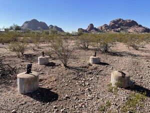 Photo showing 4 cement cylinders with metal spokes that made up the base of a guard tower in the desert, buttes of Papago park in the background
