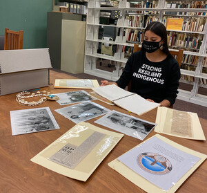 Person sitting at a table looking at photographs and documents with a bookshelf behind