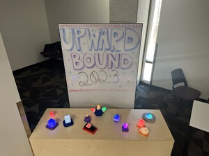 3D printed models in various colors and shapes on a table in front of an Upward Bound 2023 sign