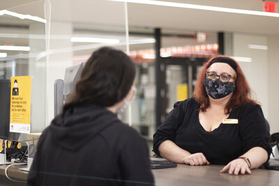 Two people wearing masks talking at the library service desk