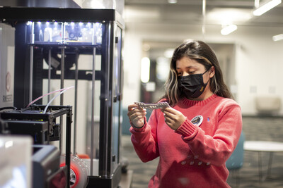A makerspace worker inspects a 3D printed ear guard design for face masks.