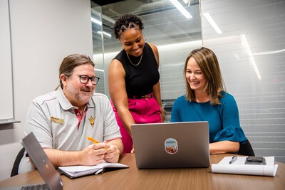 Three people talking and looking at a laptop