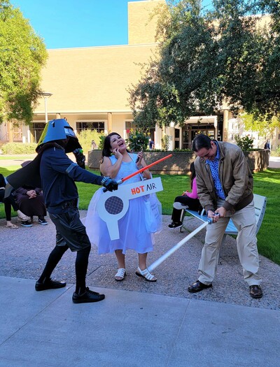 Pictured left to right: Alex Soto (Tohono O'odham) as Dark Helmet, Vina Begay (Diné) as Princess Vespa, and Eric Hardy (Diné) as Lone Starr. Dark Helmet and Lone Starr are fighting over Princess Vespa with light sabers.