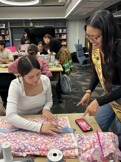 Photo of Miss Indigenous ASU helping a student measure pink fabric to cut and sew a ribbon skirt