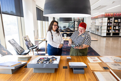 Two people standing in a room filled with sunlight in front of tables displaying archival materials