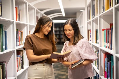 Two people standing in the stacks looking at a book together