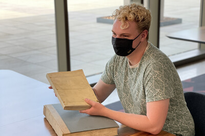 Undergraduate student wearing a mask and holding a book