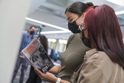 Two women wearing masks looking at a book
