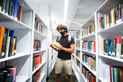 Masked-up student browsing Hayden Library book collection