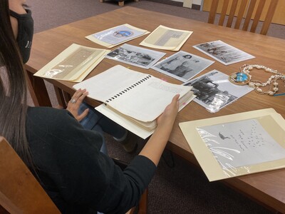 An Indigenous student examines photographs and articles preserved in archival sleeves.