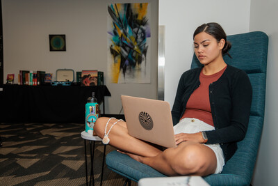 An Indigenous student works on her laptop which is resting in her lap.