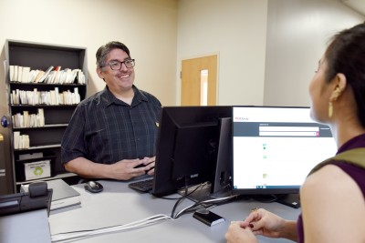 Library employee stands behind a service desk and talks to a library customer.
